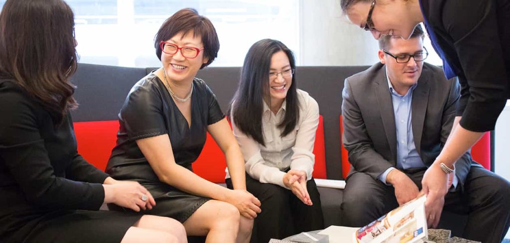 Five people sitting around a table laughing and looking at a magazine